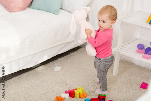 adorable kid in pink shirt holding rabbit toy in children room
