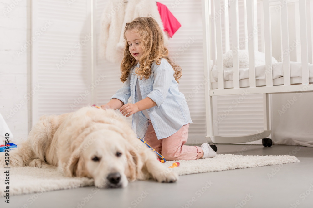 adorable kid with curly hair pretending veterinarian and examining golden retriever in children room