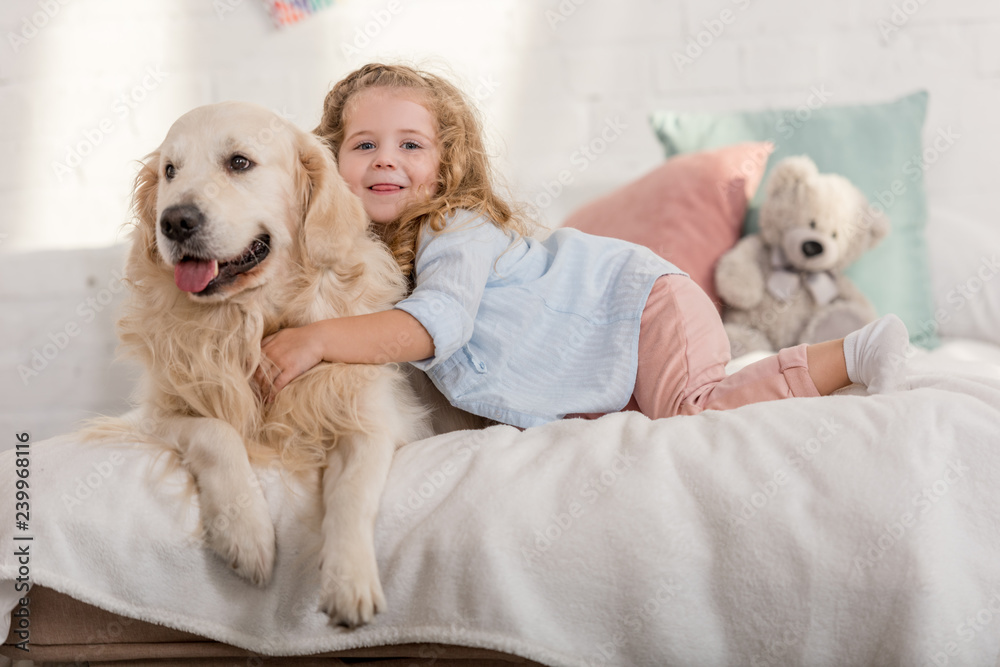 adorable happy kid and golden retriever lying on bed in children room adorable happy kid and golden retriever lying on bed in children room