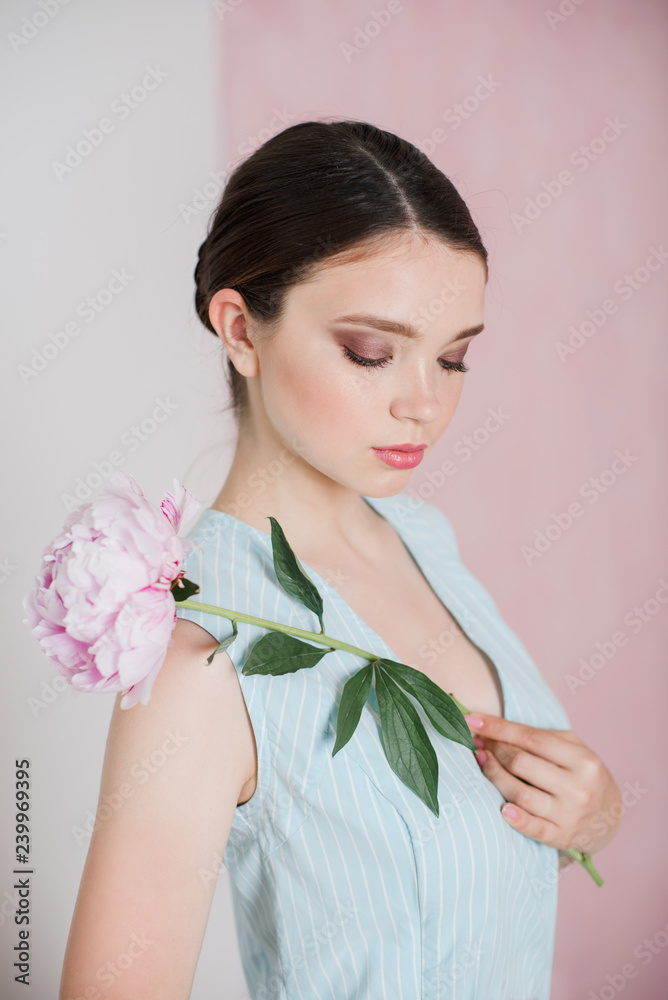 A young woman with gathered hair is standing holding a peony in her hands. A young woman with gathered hair is standing holding a peony in her hands.