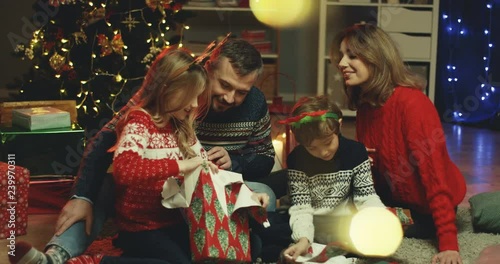 Cute Caucasian kids, sister and brother, unpacking their x-mas presents from Santa Claus together with their parent snear the Christmas tree in the living room. photo