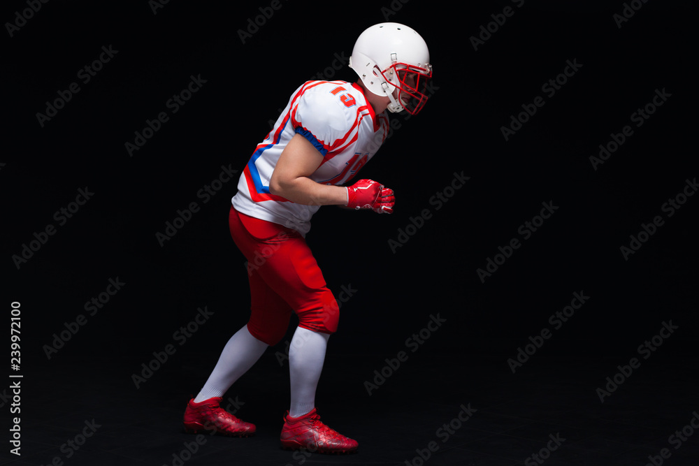 Side view of American football player wearing helmet taking position while playing against black background
