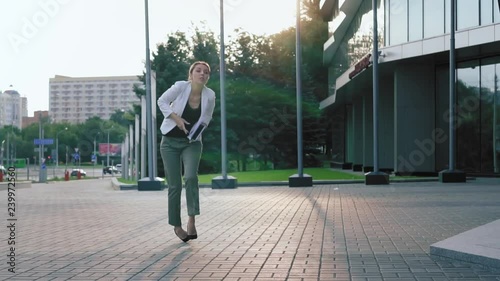 Business woman in high heels walks down the street, stumbles, drops documents, and puts them in order. Fail. Slow motion photo