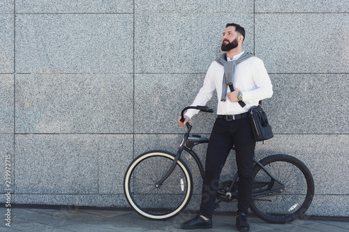 Businessman standing against building wall with his bicycle.