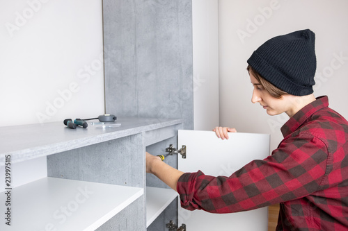 Woman adjusting furniture door in a new living room cabinet. Female in casual shirt and knit hat does "men" carpenter work at home