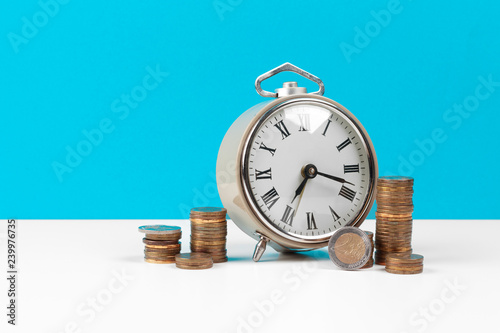 Alarm clock and money coins on the table.