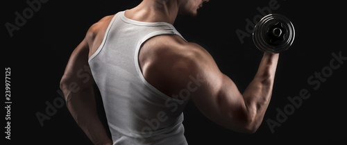 Strong athletic man with dumbbell showes muscular body