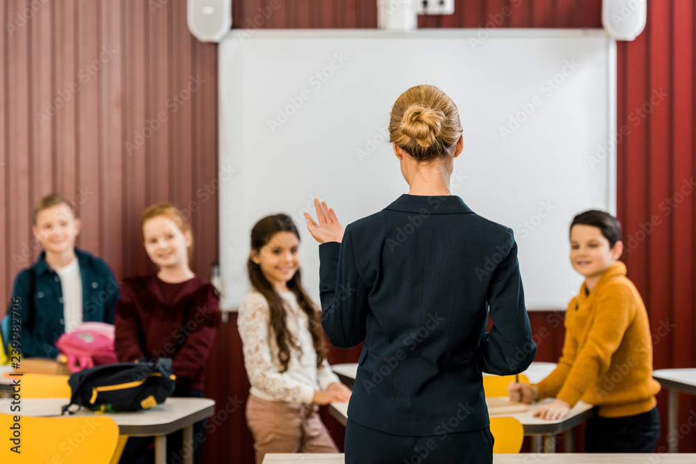 Fototapeta premium back view of teacher talking with smiling schoolchildren