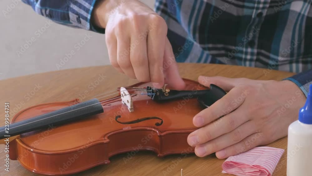 Close-up hands of young man in plaid shirt is repairing a violin sitting at the table.