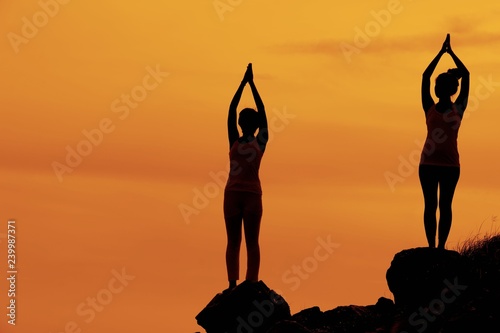 Two Yoga women are doing yoga during Sunset on the cliff