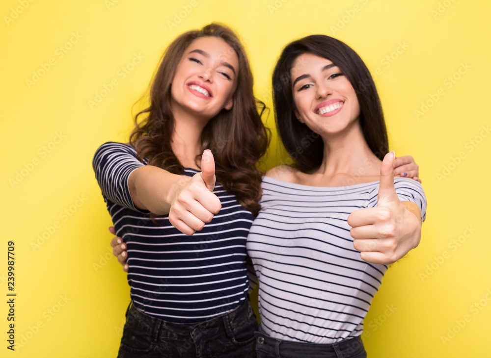 Cute women friends showing thumbs up on yellow background Cute women friends showing thumbs up on yellow background