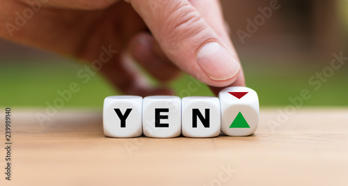 Hand is turning a dice and changes the direction of an arrow symbolizing that the value of the Yen is going up (or vice versa)