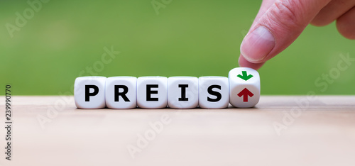 Hand is turning a dice and changes the direction of an arrow symbolizing that the price ("Preis" in german) is going down (or vice versa)
