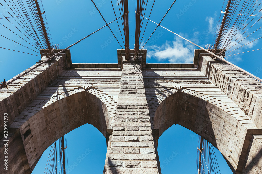Fototapeta premium widok z dołu na brooklyn bridge na niebieskim tle pochmurnego nieba w nowym jorku, usa