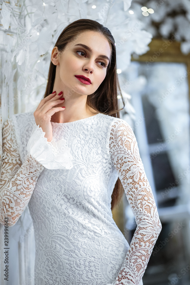 Fototapeta premium Fashion portrait of beautiful young woman in a gorgeous wedding dress, posing in a fantasy interior with white winter tree