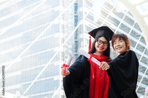 Two girls in black gowns and hold diploma certificate with happy graduated.