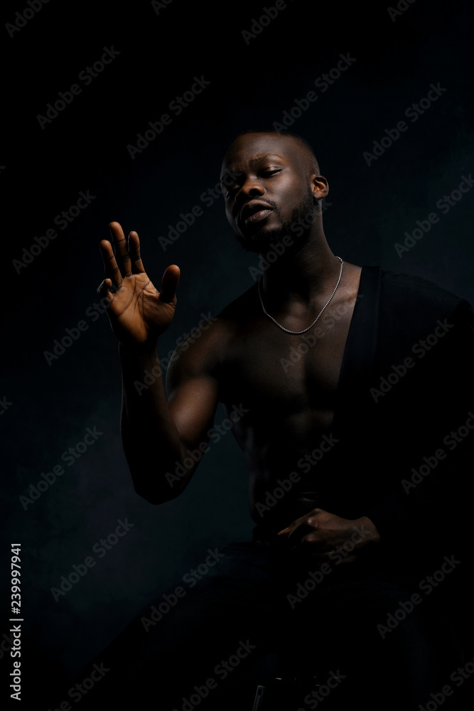 Dark key portrait of sexy musician man topless, with jacket on one shoulder. Studio shot, black background