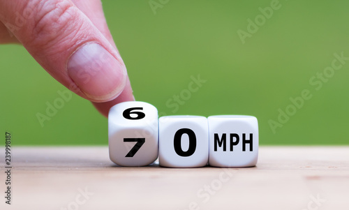 Hand is turning a dice and changes the expression "70 MPH" to "60 MPH" as symbol to reduce the speed limit from 70 to 60 miles per hour