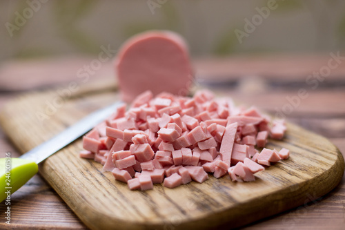 Chopped boiled sausage on a wooden board.