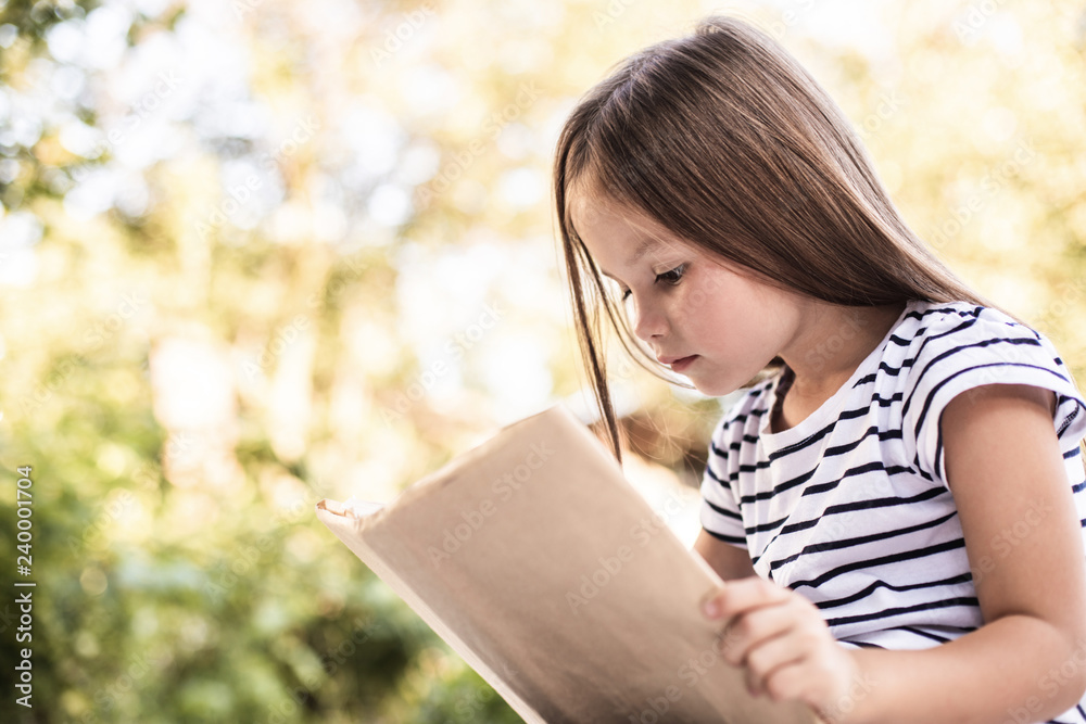 Obraz premium Little girl mindfully reading book in park