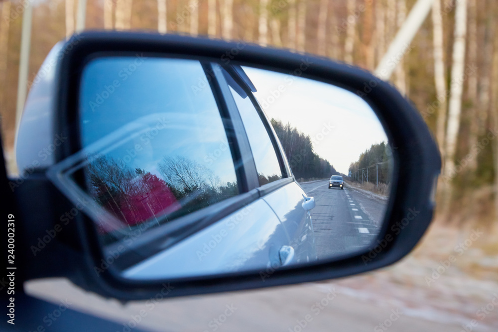 Side mirror of the car and the reflection of the road in it. Autumn landscape