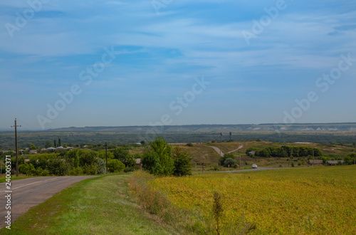 Blue sky with beautiful clouds over the countryside. In the distance, one-story buildings are visible. Summer.