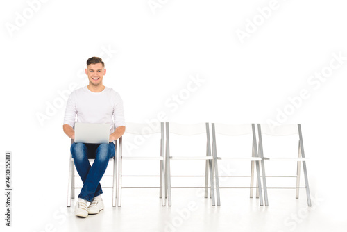 handsome young man sitting with crossed legs and laptop isolated on white
