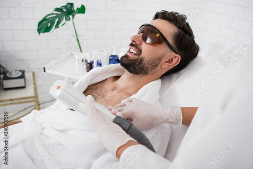 Happy man wearing laser safety goggles during hair removal procedure photo