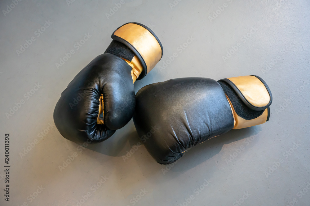 Old black and yellow boxing gloves on grey concrete background.
