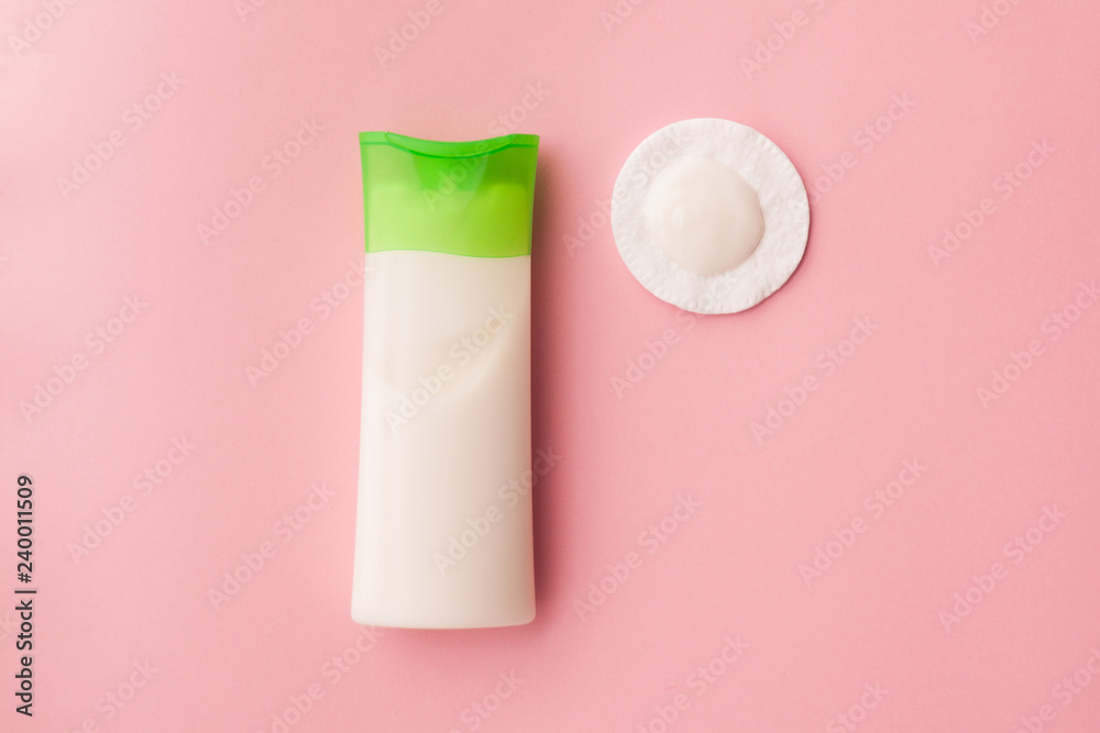 cleansing cream for the face and a cotton pad with a remuver. pink background. makeup removal. skin care. top view. selective focus.