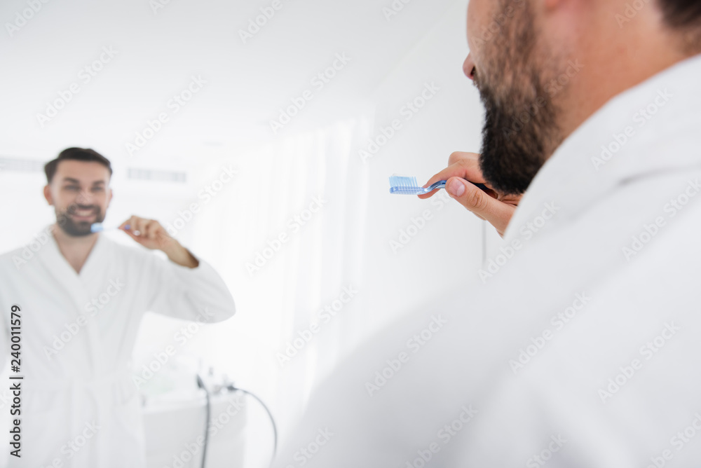 Mirror reflection of the man brushing his teeth