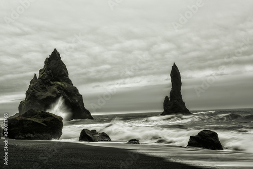 A beach with volcanic sand and rocks sticking out of the water. Black and white photo. Stormy Ocean. Iceland. Beach Vic. 
 photo