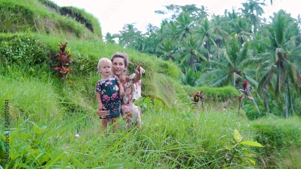 beautiful young mother with a child of 2 years in her arms looking at the camera and smiling against the green palm trees on the island of Bali in the tropics beautiful young mother with a child of 2 years in her arms looking at the camera and smiling against the green palm trees on the island of Bali in the tropics