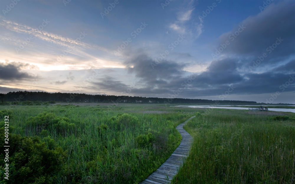 A wooden boardwalk spans a marsh in the Outer Banks, North Carolina, at sunset