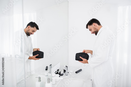 Waist up of positive man standing with his toiletry bag