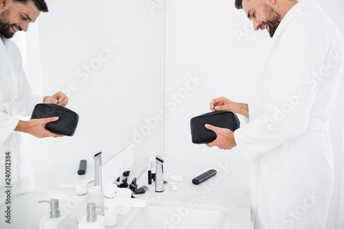 Happy bearded man smiling while opening toiletry bag