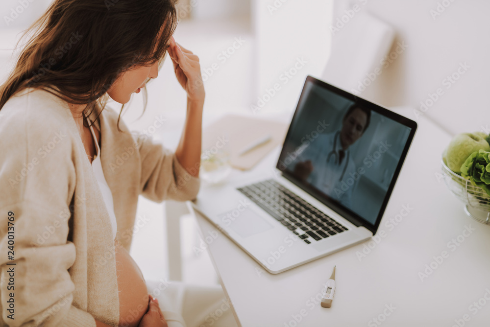 Unhappy tired woman sitting behind table with online video call from doctor Unhappy tired woman sitting behind table with online video call from doctor