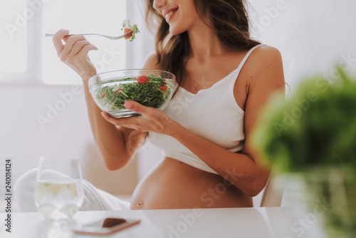 Smiling woman eating fresh salad on bright kitchen