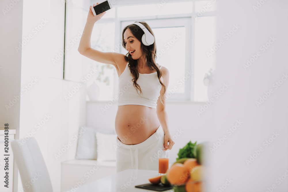 Future mom in headset holding cellular in hand and dancing Future mom in headset holding cellular in hand and dancing