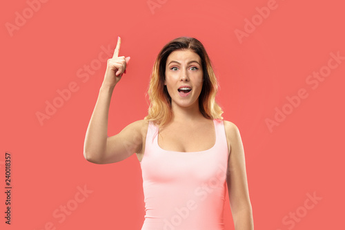 Wow. Beautiful female half-length front portrait isolated on coral studio backgroud. Young emotional surprised woman standing with open mouth. Human emotions, facial expression concept. Trendy colors