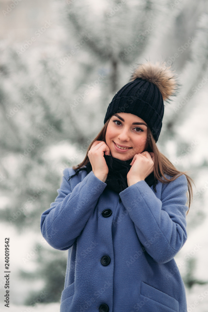 Portrait of happy young woman wearing winter hat and scarf stands next to the Christmas tree Portrait of happy young woman wearing winter hat and scarf stands next to the Christmas tree
