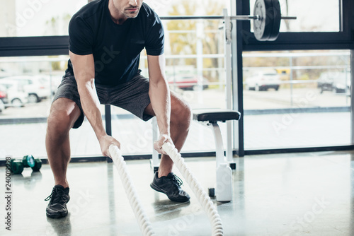 cropped image of sportsman working out with ropes in sport center