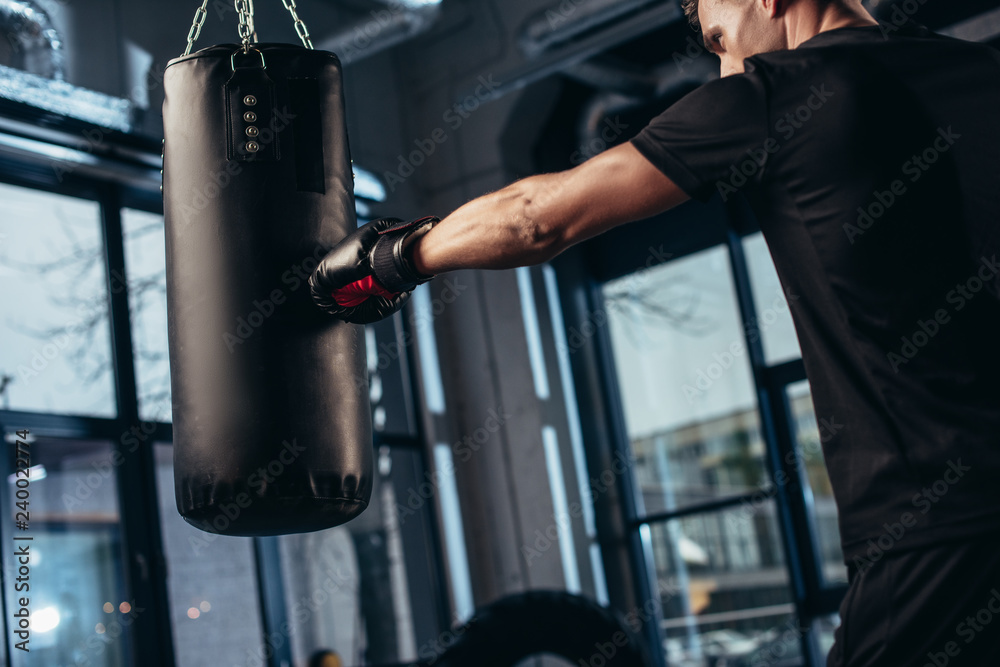 side view of handsome boxer training with punching bag in gym