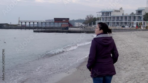 4K Shot from back. The woman appears from behind the camera and walks along the spring beach photo