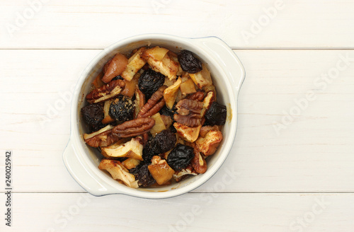 White baking form with apple baked pudding with dark raisin, pecan nuts, cinnamon and sugar on white wooden background