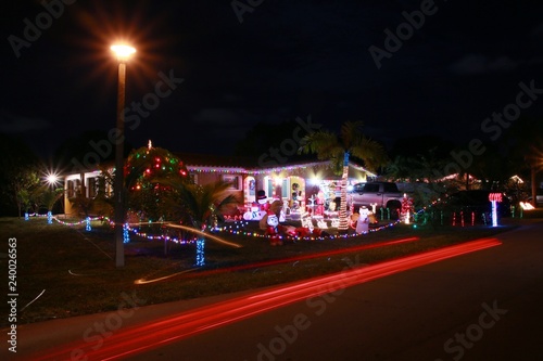 House Adorned with Christmas Holiday Decorations including Trees Santa Elves and Snowmen with Car Lights Streaking by in the Foreground in a Long Time Exposure at Night © kthx1138
