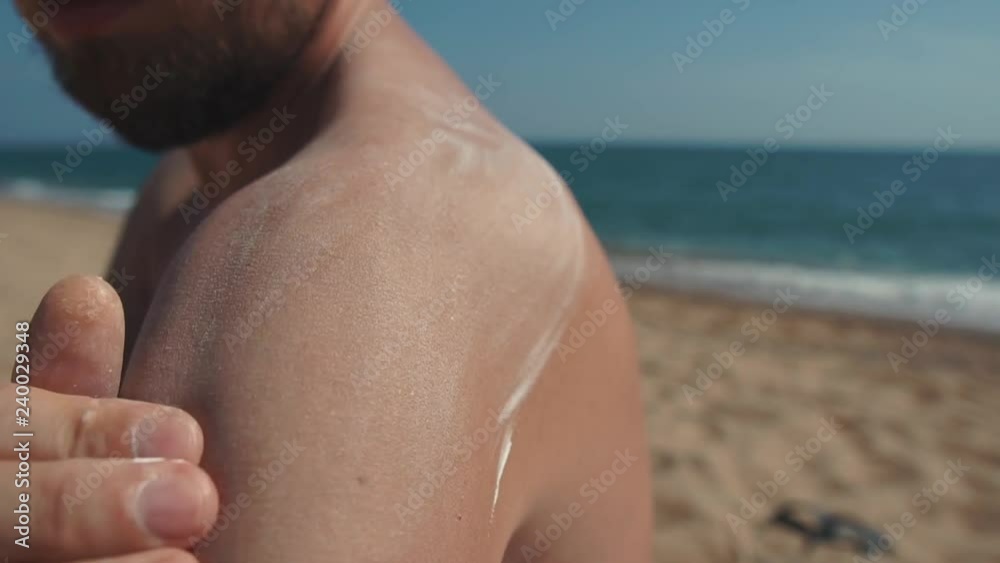 Male holidaymaker is rubbing shoulder, applying sunblock on a beach, close-up Male holidaymaker is rubbing shoulder, applying sunblock on a beach, close-up
