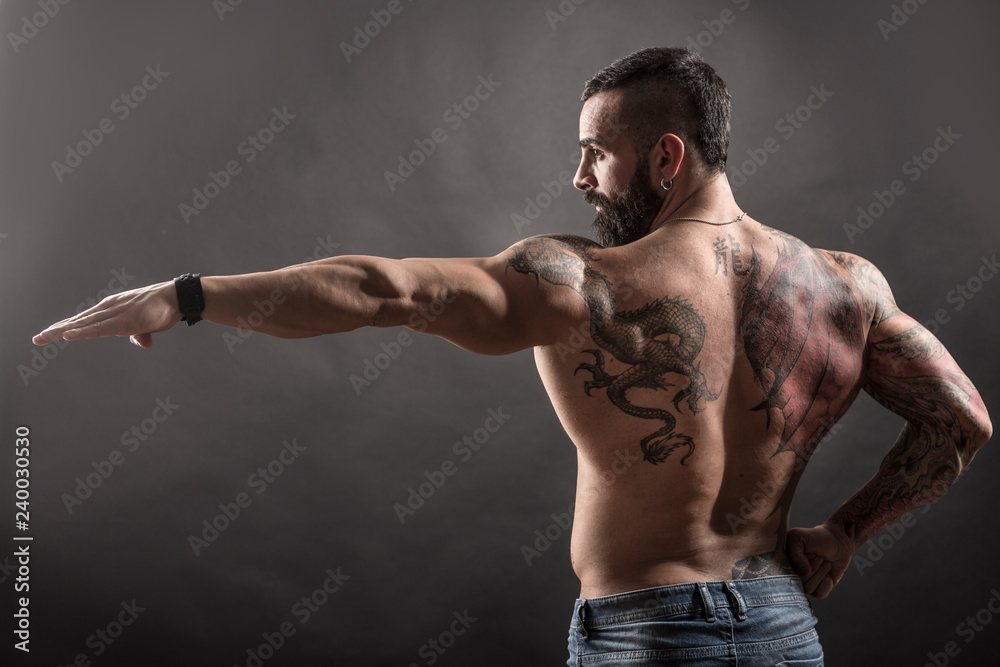 Uomo muscoloso e tatuato in posa plastica - obrazy, fototapety, plakaty 