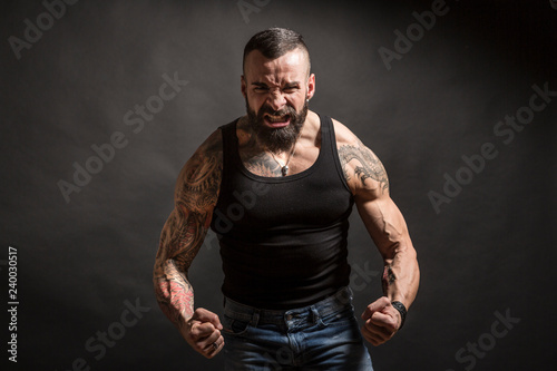 Uomo muscoloso e tatuato con faccia molto arrabbiata e muscoli in tensione photo