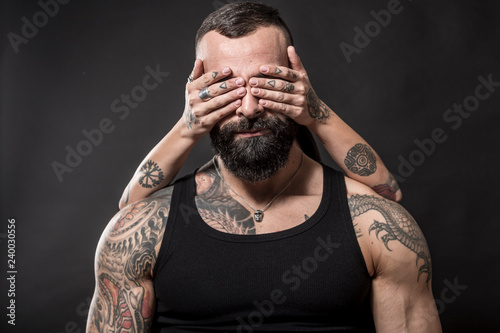 Uomo muscoloso e tatuato in primo piano e mani  tatuate che gli coprono gli occhi photo